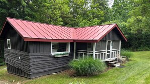Une petite cabane avec un toit rouge, une véranda et une fenêtre à cadre blanc.
