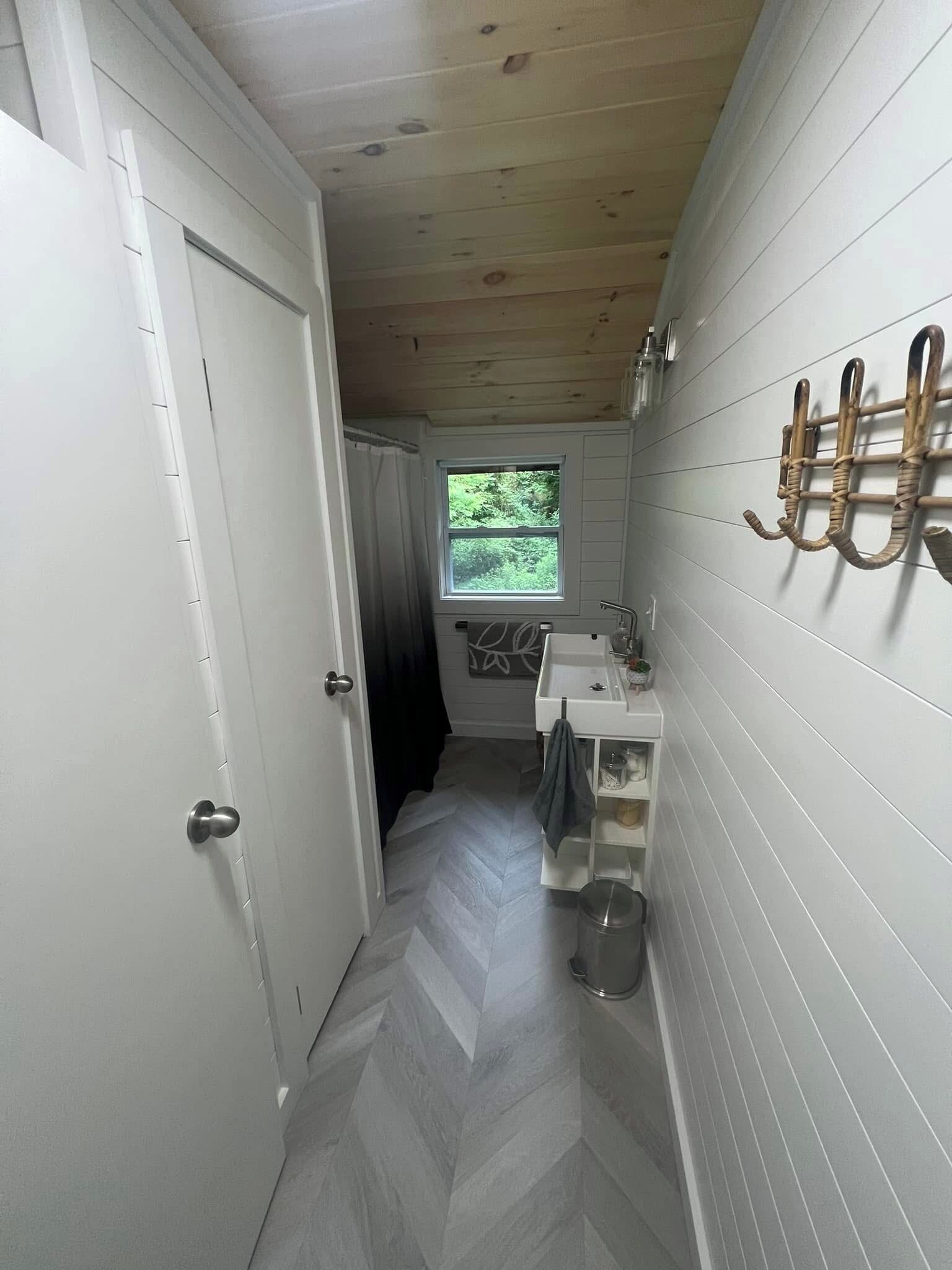 A narrow hallway with a wooden ceiling, a white door, and a window with a view of greenery.