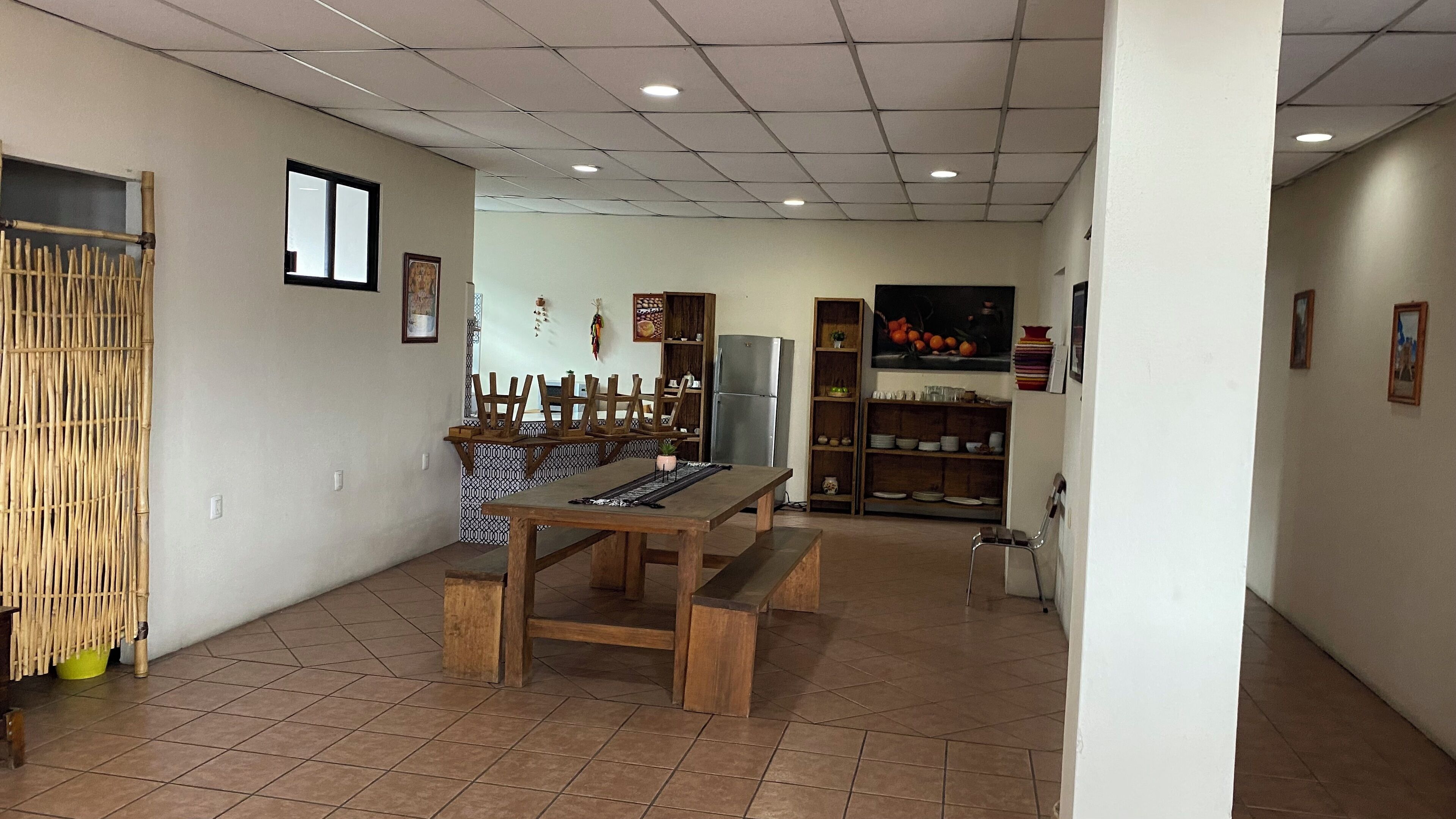 Un coin repas avec une table et des bancs en bois, un réfrigérateur, ainsi que des étagères où sont rangés de la vaisselle et des objets de décoration.