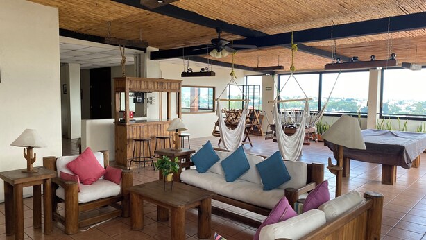 A spacious living area with a wooden ceiling, a sofa with blue and purple cushions, a coffee table, and a bar area with a mirror and bar stools. - Casa Lucia Oaxaca (Oaxaca)