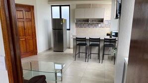 A modern kitchen with a refrigerator, a dining area with a glass table, and a bar area with chairs. - Casa Lucia Oaxaca (Oaxaca)
