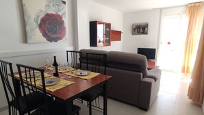 A dining area with a table set for four, a sofa, a television, and a painting on the wall.
