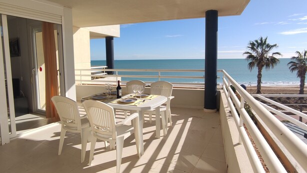 A balcony with a table set for dining, overlooking a beach.