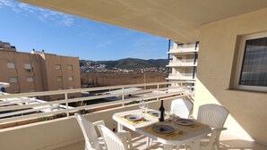 A balcony with a table set for dining, white chairs, and a view of buildings and hills in the distance. - Apartamento Picasso 3 Inmomart (Peñiscola)