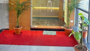 Entrada de hotel con alfombra roja, fachada de madera y plantas en macetas.