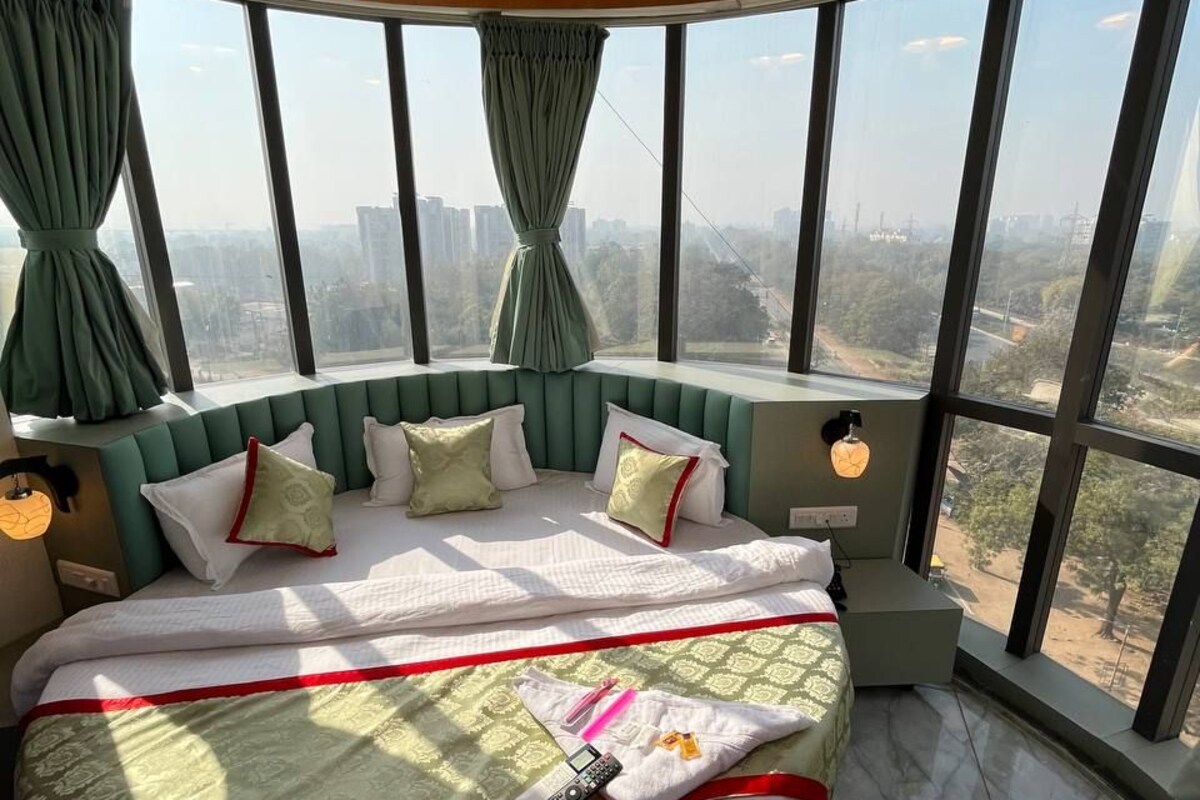 Habitación de hotel en un rascacielos con una cama curvada, ventanas amplias y vistas a la ciudad.