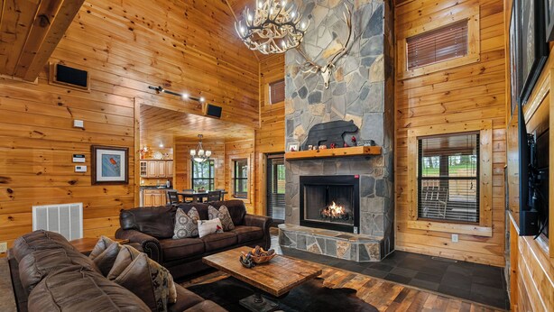 A cozy cabin interior with a stone fireplace, wooden walls, leather sofas, and a dining area. - You have to see Red Bird Lodge (SEVIERVILLE)