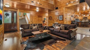 A spacious wooden cabin interior with a living area featuring leather sofas, a coffee table, and a fireplace. - You have to see Red Bird Lodge (SEVIERVILLE)