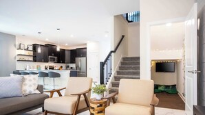 Een moderne woonkamer met een bank, twee fauteuils, een salontafel en een televisie op de achtergrond.