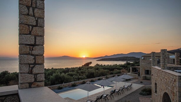 A stone building with a pool and lounge chairs overlooking a sunset over the sea. - Dream Villas (West Mani)