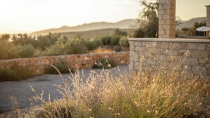 A stone wall with a pergola structure, surrounded by dry grass and shrubs, with a mountainous landscape in the background. - Dream Villas (West Mani)