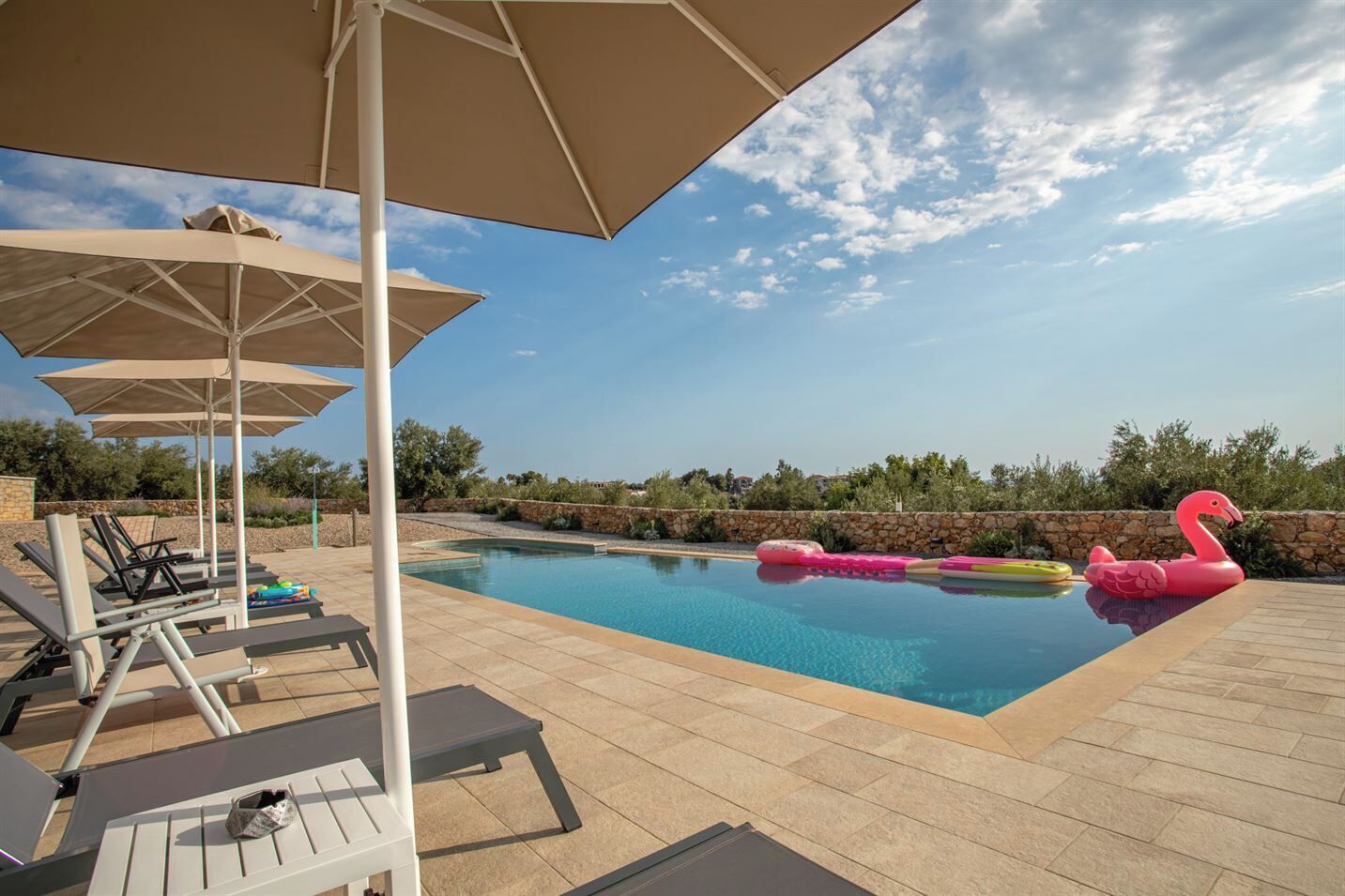 Una piscina con sillas de descanso y sombrillas, rodeada de muros de piedra y vegetación.