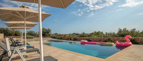 Una piscina con sillas de descanso y sombrillas, rodeada de muros de piedra y vegetación.