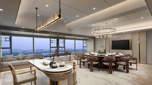 A spacious living area with a large dining table, comfortable seating, a modern chandelier, and a large window offering a city view. - Ramada by Wyndham Foshan Danzao (Foshan)