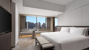 A modern hotel room with a large bed, a TV, a seating area with a table, and a view of the city skyline. - Ramada by Wyndham Foshan Danzao (Foshan)