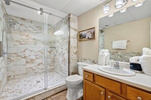 Un baño con ducha envuelta en vidrio, inodoro, lavamanos con espejo y tocador de madera.