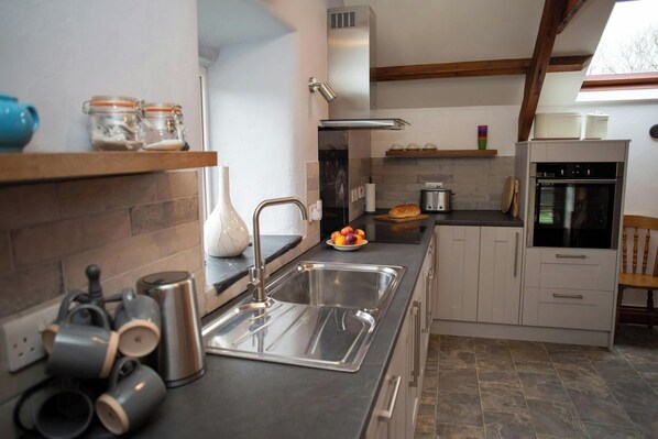 A modern kitchen with a sink, stove, and oven, featuring a stone tile backsplash and wooden beams.