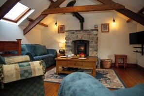 A cozy living room with a stone fireplace, wooden beams, a sofa, and a television.