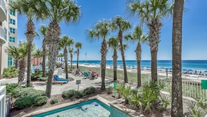 A pool area with palm trees, a beach view, and a building with balconies. - Open Oct 25–Nov 2! Beautiful Condo Near Pier Park! (Panama City Beach)