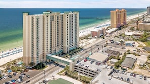A high-rise hotel with multiple floors, a parking lot, and a beach in the background. - Open Oct 25–Nov 2! Beautiful Condo Near Pier Park! (Panama City Beach)