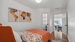 A bedroom with a bed, a chair, and a door leading to a dining area. - Cozy 1BDR APT in Vibrant Downtown Geneva (Geneva)