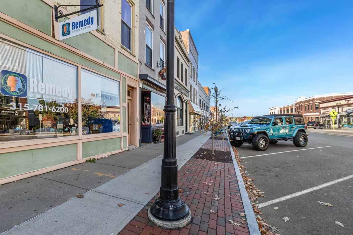 A street view with a building labeled 'Remedy' and a parked blue Jeep on the sidewalk.