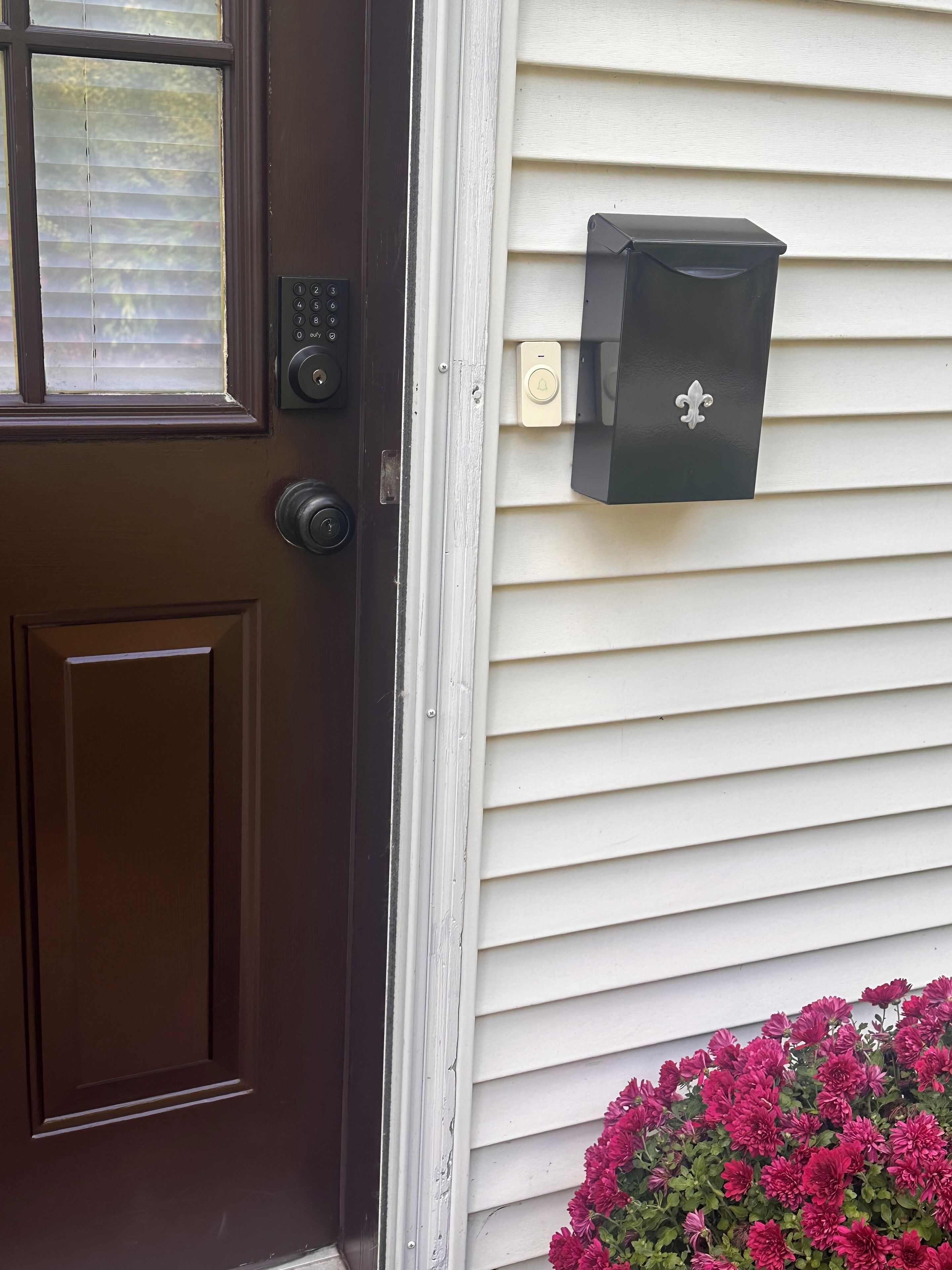 A brown door with a keypad lock, a mailbox, and a flower box with pink flowers.