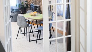 An open door leading to a dining area with a table set for two, a potted plant, and a stone wall in the background. - SOFIMA-Cozy and Charming 2-bedroom apartment! (Woburn)