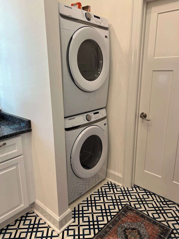 Un cuarto de lavandería con lavadora y secadora apiladas, una puerta y piso estampado.