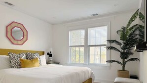 A bedroom with a large bed, a bedside table, a mirror, and a potted plant.