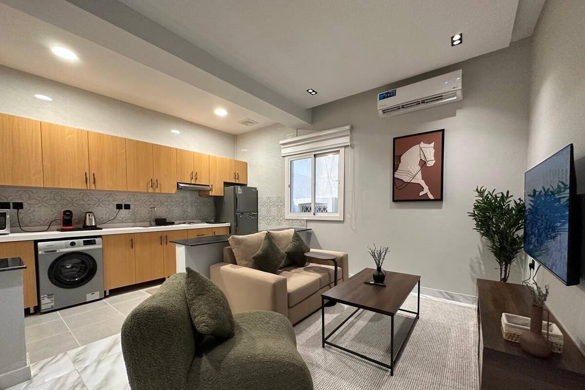 A modern kitchen with wooden cabinets, a washing machine, and a dining area with a sofa and coffee table.