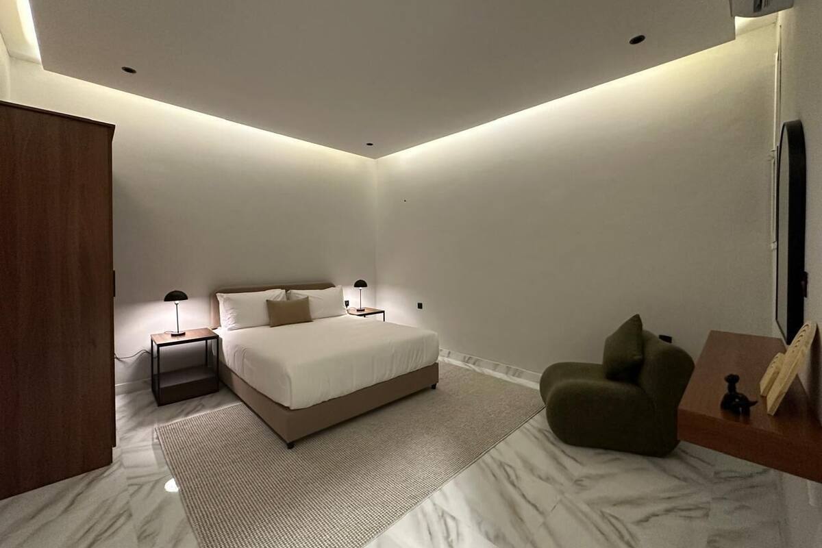 A modern bedroom with a bed, bedside tables, a green chair, and a small wooden side table.