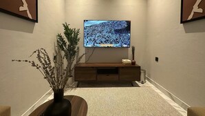 A hallway with a flat-screen TV mounted on the wall, a wooden console table, and a textured rug. - M-Residence by Dayf Self-Service Apart. (Jeddah)