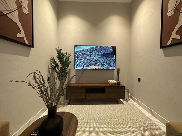 Un corridoio con una TV a schermo piatto montata a parete, un tavolino consolle in legno e un tappeto con trama decorativa.
