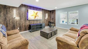 Una sala de estar moderna con un televisor grande, sofás de cuero, una pared decorativa de madera y vistas al exterior.