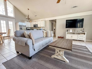A spacious living area with a grey sofa, a wooden coffee table, and a TV on the wall.