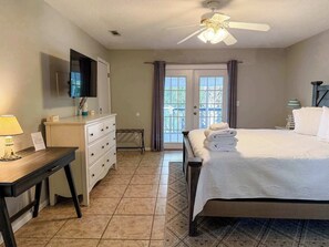 A hotel room with a bed, a desk, a dresser, a ceiling fan, and a TV.