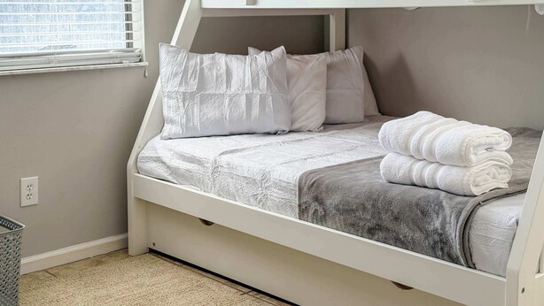 Uma cama beliche com roupa de cama branca, almofadas, um cobertor cinza e uma toalha enrolada.