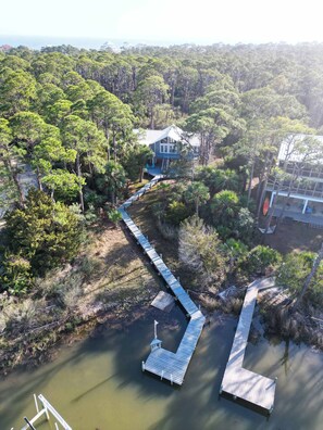 An aerial view of a house surrounded by dense forest, connected to a dock extending into a body of water.