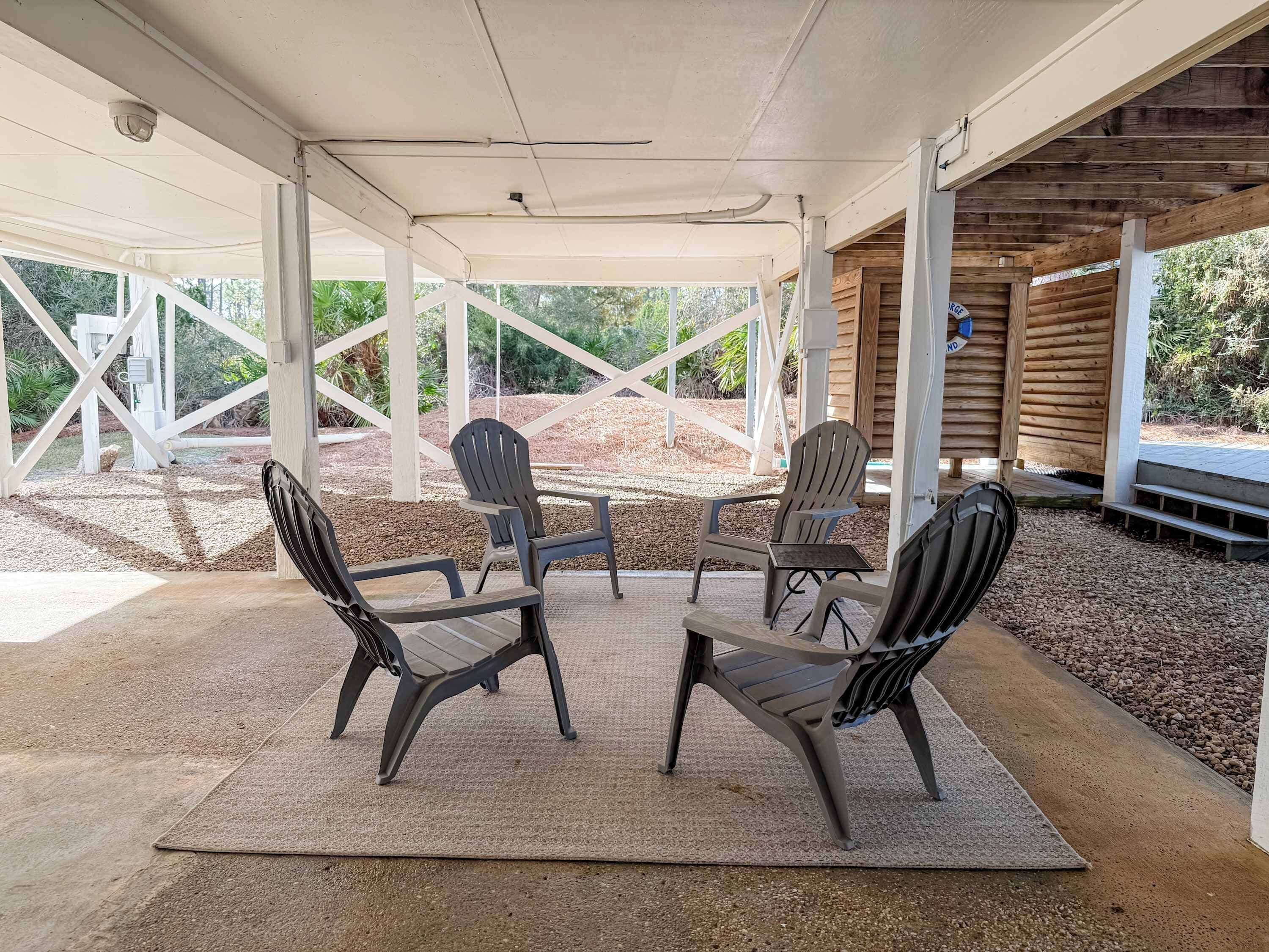 A covered outdoor seating area with four chairs and a table, surrounded by a gravel floor and white structural beams.