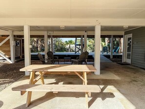 Portico esterno coperto con tavolo e sedie in legno, circondato da pilastri in cemento.
