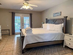 A neatly made bed with a white comforter and pillows, a wooden headboard, a nightstand with a lamp, and a view of the outdoors through a glass door. - Canal Front Pet Friendly Boat Dock St George Island-Beach access (Eastpoint)