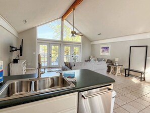 Una cucina con un lavello doppio, una zona pranzo con tavolo e sedie, e un'ampia finestra vista all'esterno.