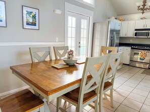 A dining area with a wooden table and white chairs, a kitchen with white cabinets and stainless steel appliances, and a framed picture on the wall. - Canal Front Pet Friendly Boat Dock St George Island-Beach access (Eastpoint)