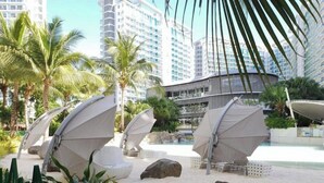 A resort area with outdoor seating and umbrellas, palm trees, and a pool.