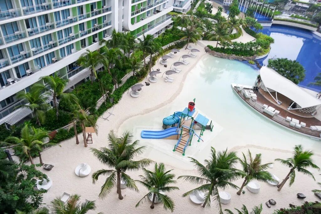 A resort with a pool area, palm trees, and a children's play structure.