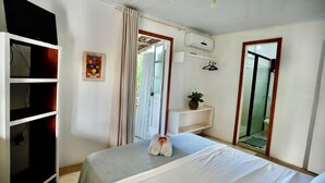 Een hotelkamer met een bed, een kledingkast, een airconditioning, een klein plankje met een plantje en een spiegel.