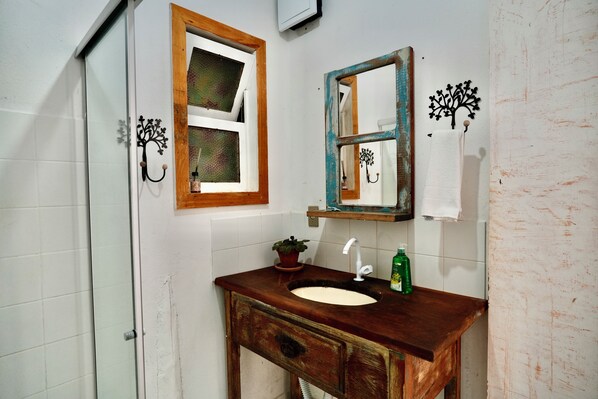 Un baño con tocador de madera, lavamanos blanco, espejo decorado con un árbol y un perchero para toallas.