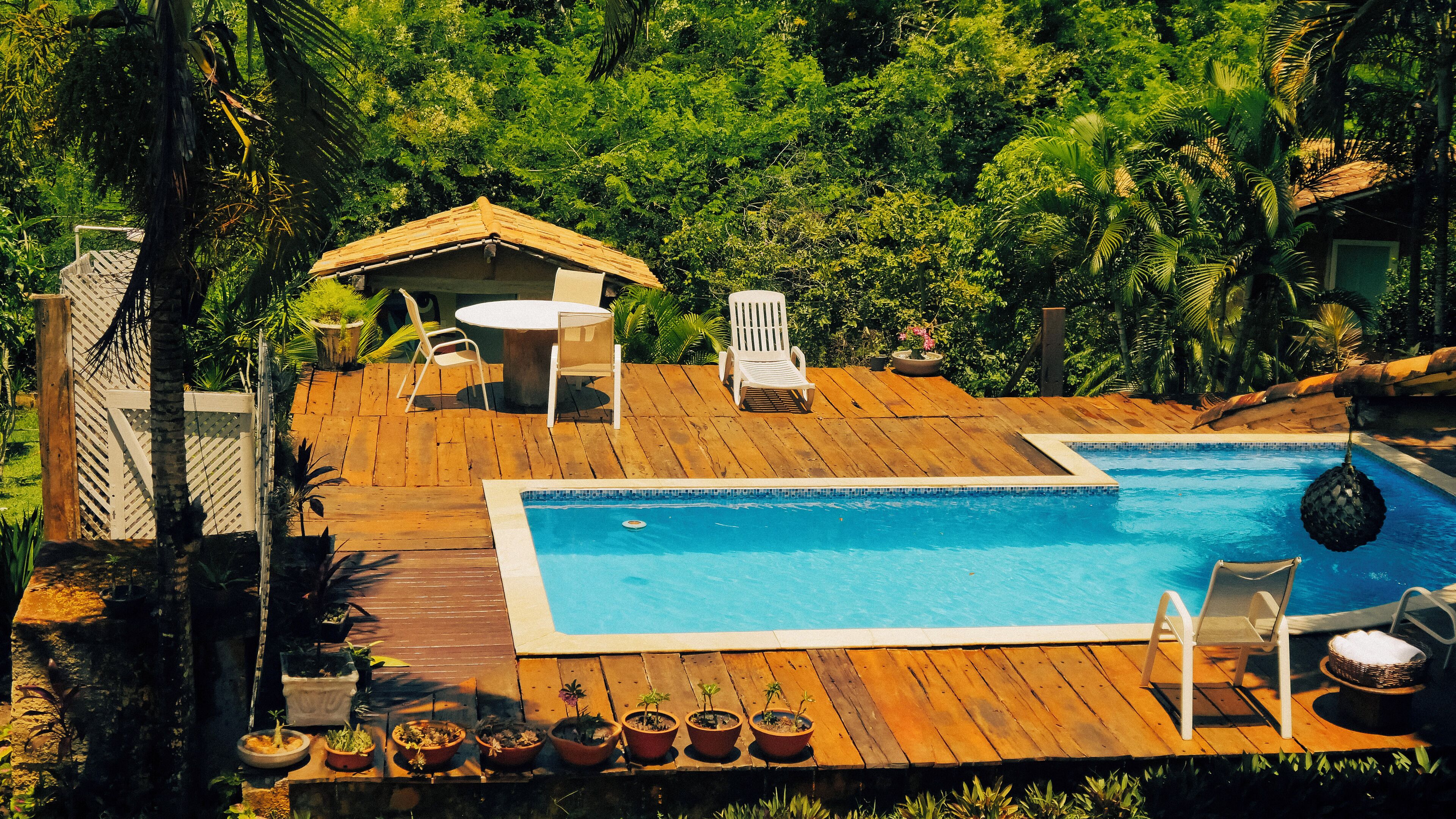 Une terrasse en bois avec une piscine, entourée d’une végétation luxuriante et agrémentée d’un petit kiosque.