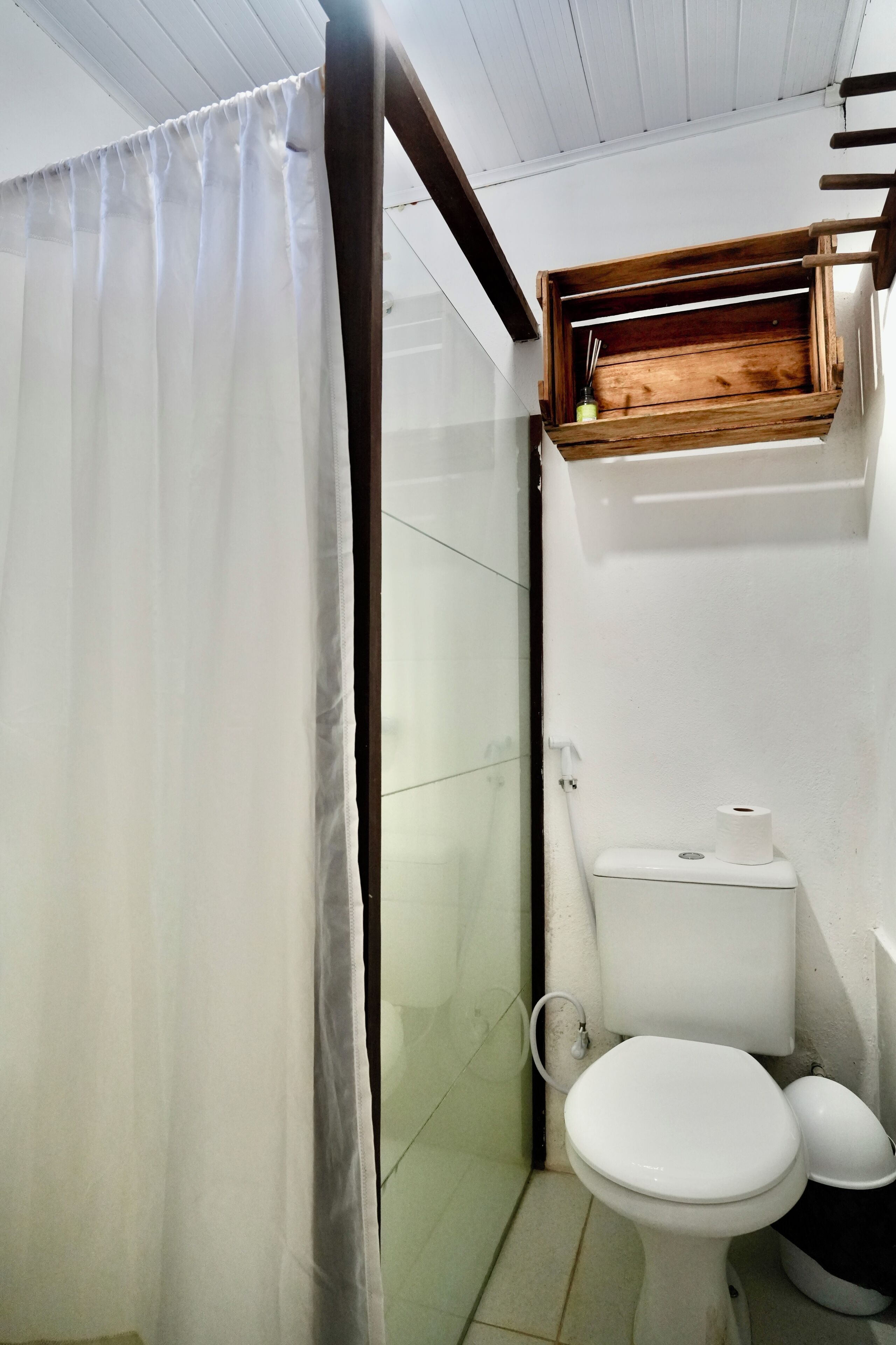 Une petite salle de bain avec des toilettes, une étagère en bois au-dessus des toilettes et un rideau de douche.